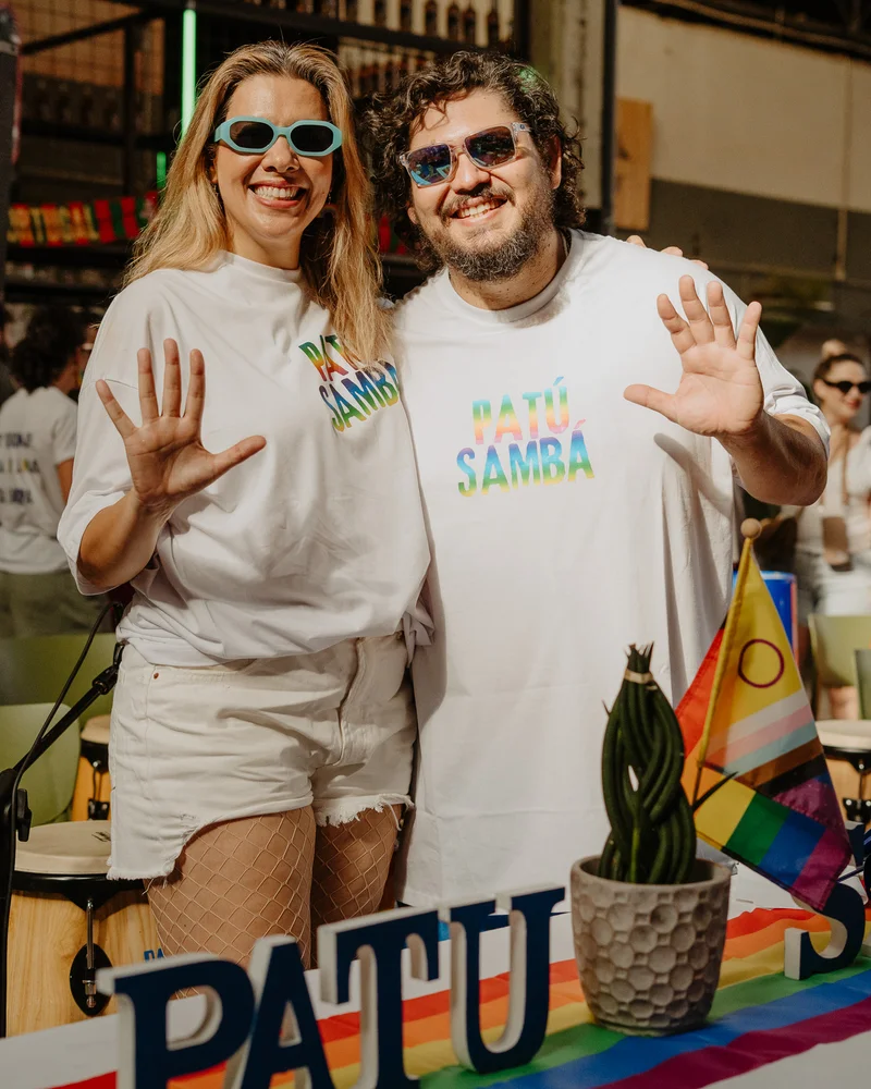 Duas pessoas com camisolas do Patú Sambá a sorrir e acenar